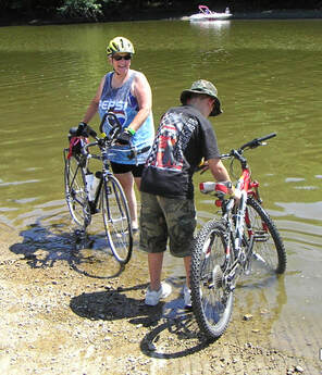 A woman and young boy dip their tires in the shores of the Mississippi River after completing RAGBRAI
