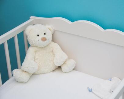 A white teddy bear sits in a white baby crib 