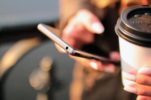 Person holding smartphone in one hand, coffee in the other